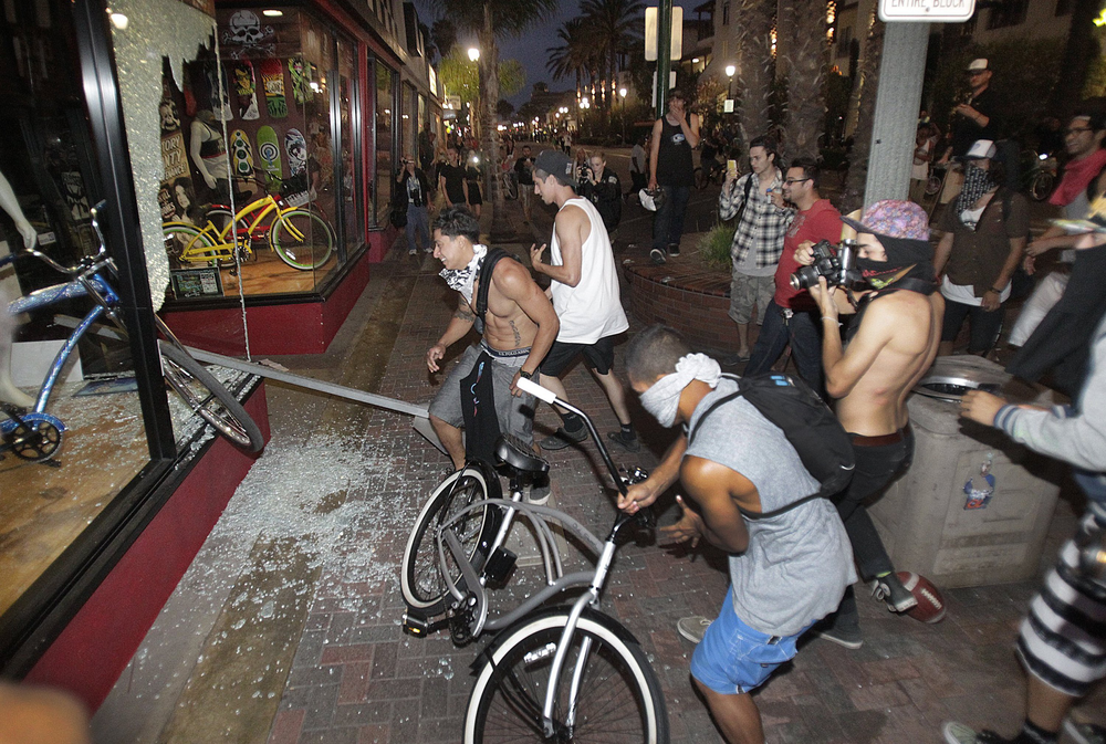 Rioters celebrate, loot and steal a bike after smashing a stop sign through the windows of Easyrider business on the corner of Main and Orange Streets downtown Main Street in Huntington Beach, Calif. on July 28.