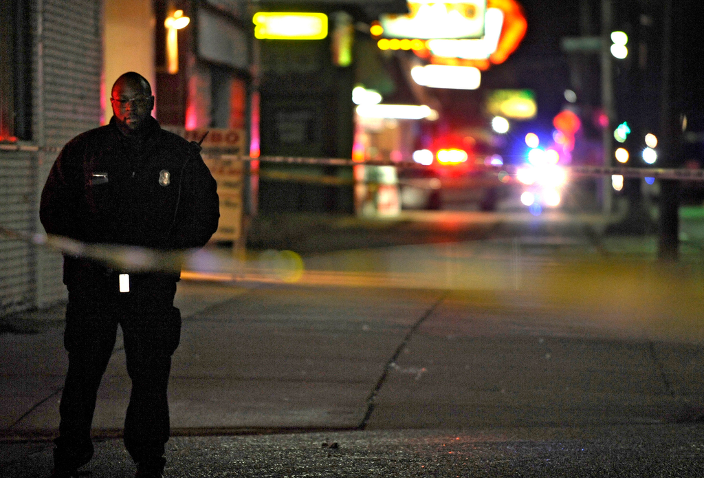 A Detroit Police officer stands guard behind barrier tape at the scene of a shooting which left three dead at a barbershop on Nov. 6, 2013.
