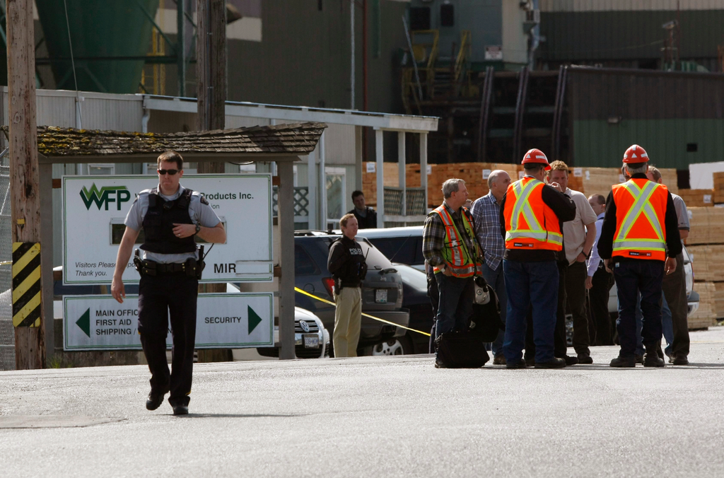 Mill workers talk as a police officer walks away following a shooting at Western Forest Products in Nanaimo, British Columbia on April 30.