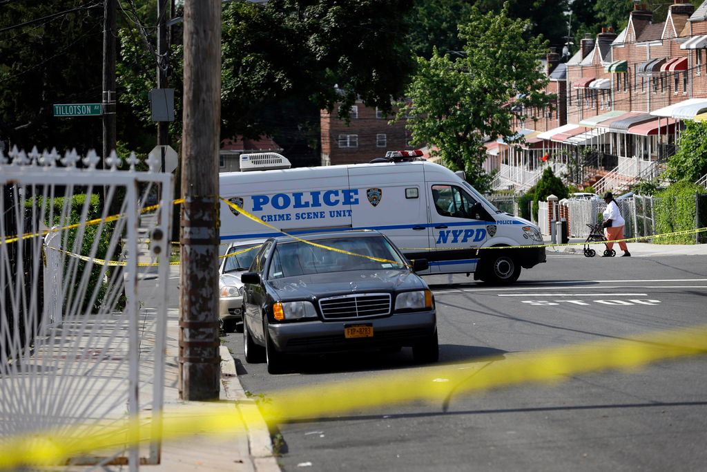 A woman walks past a crime scene where police discovered a man who had been shot and subsequently died, in the Bronx section of New York on June 30.