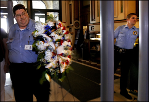 Illinois Secretary of State security guard Carl Faust, left, carries a wreath of flowers around the metal detector at the north entrance of the Illinois state Capitol in Springfield, Ill. He is joined by Mitch White of ELA Security, who is working the fac