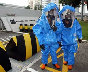 Firefighters wearing protection suit prepare to proceed into the Singapore embassy, background, after the embassy received a suspicious large envelope addressed to the ambassador, bearing a postmark from Malaysia's northeastern Kelantan state in Kuala Lum