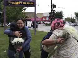 Following a shooting that left four people injured at an ice cream shop across the street from Carl Schurz High School, Sandra Acebedo, left, hugs and greets Norma Rios Sierra, as Juliet De Jesus Alejandre, right, back to camera, is greeted and hugged by a parent of high school student Monica Espinoza, who was handing out flowers to students, parents and staff on Thursday, Aug. 25, 2022. . Following a shooting that left four people injured at an ice cream shop across the street from Carl Schurz High School, Sandra Acebedo, left, hugs and greets Norma Rios Sierra, as Juliet De Jesus Alejandre, right, back to camera, is greeted and hugged by a parent of high school student Monica Espinoza, who was handing out flowers to students, parents and staff on Thursday, Aug. 25, 2022. .