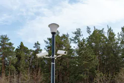 Surveillance cameras mounted on a lamppost at the side of a forest road. Surveillance cameras mounted on a lamppost at the side of a forest road.