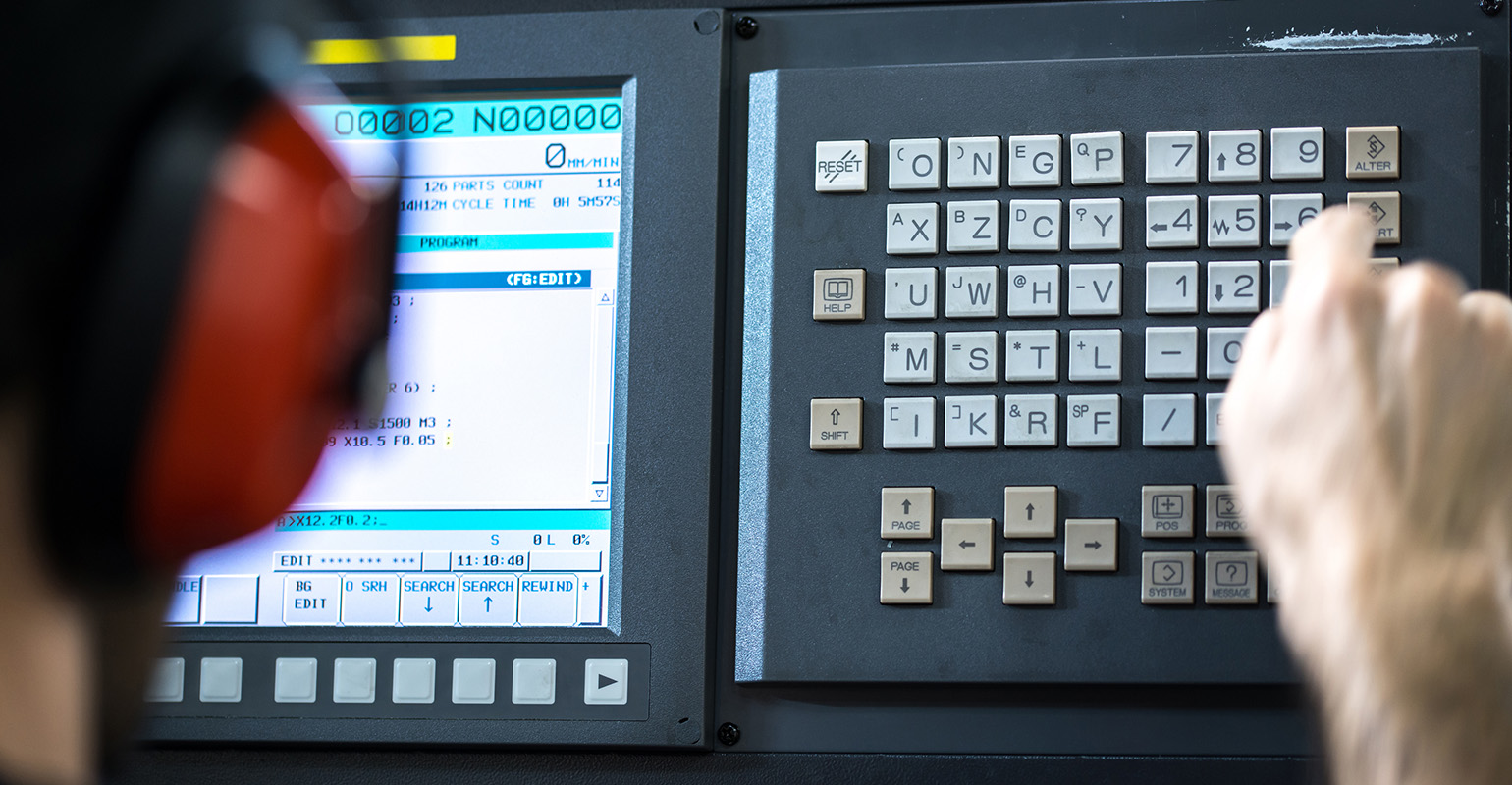 CNC operator, at milling machine center, installing data at a keyboard.