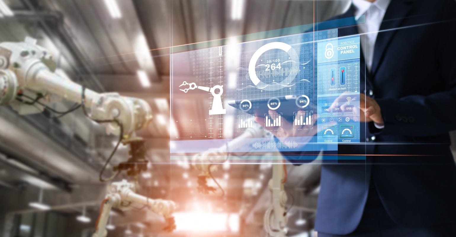 Manager / industrial engineer using a tablet checks and controls automation robot arms and machines in an intelligent factory.