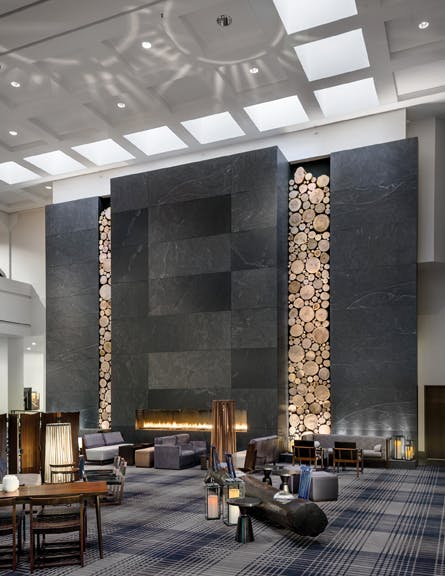 A ceiling-high stone fireplace framed by rustic wooden logs was created by artisans for the Hyatt Regency Minneapolis. Elsewhere