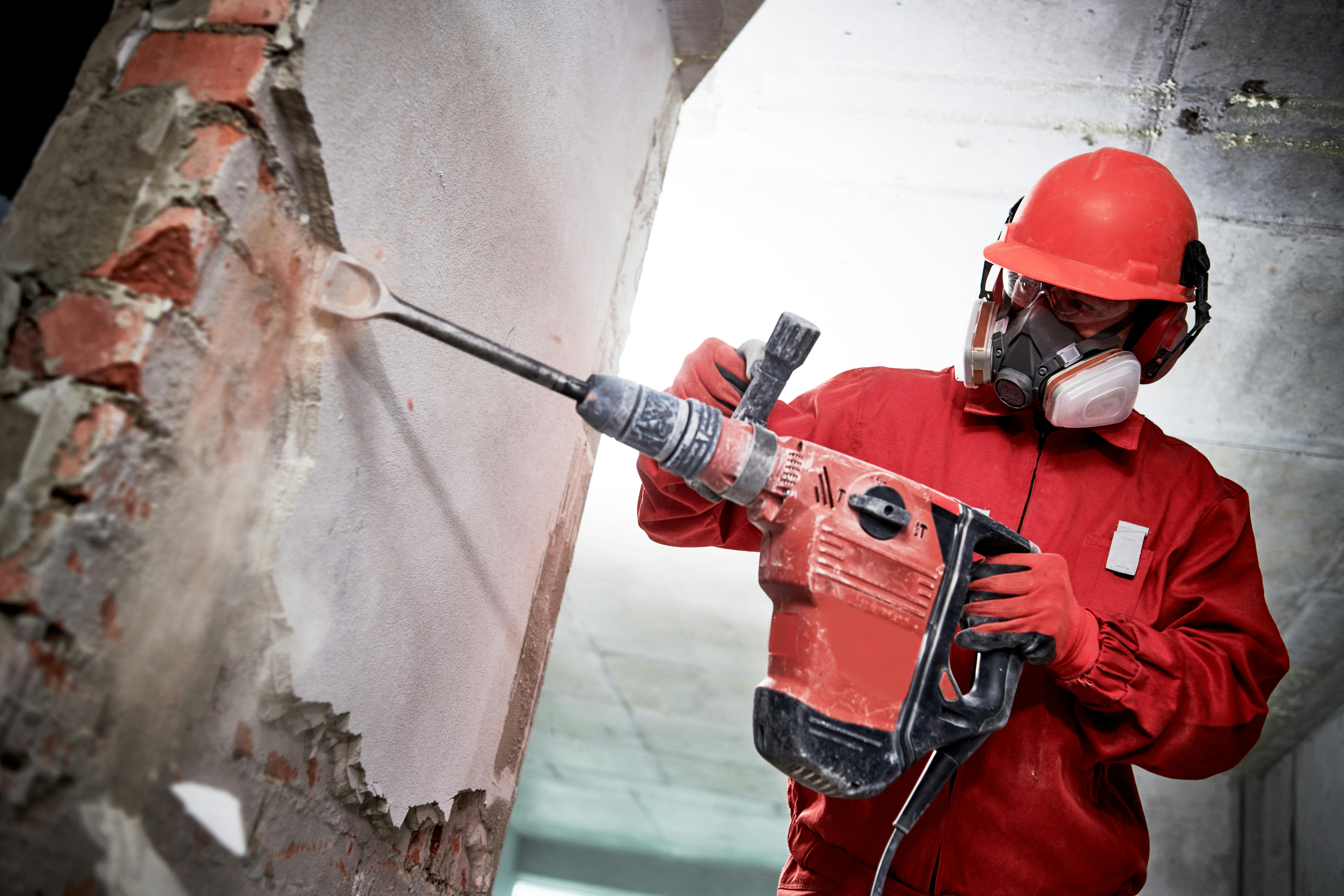 Demolition and construction destroying. worker with hammer breaking interior wall plastering. Demolition and destroying. Worker with demolition hammer in personal protection equipment removing interior brick wall plastering