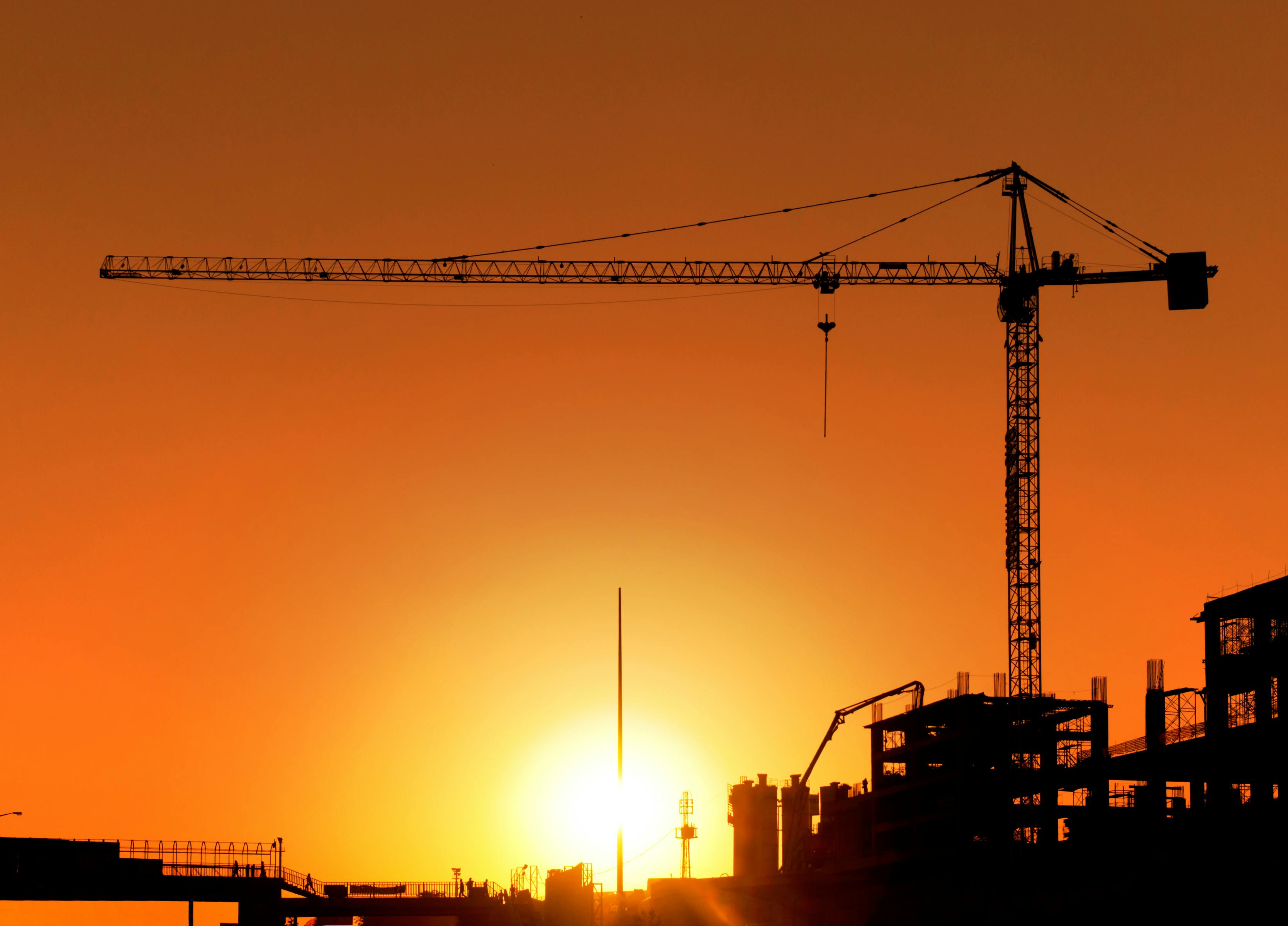 Construction Site and Crane. Horizontal photo of a construction site including a crane at sunset. The area is totally orange colored and all the buildings and equipment is seen as a silhouette