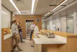 The cafe area is a destination for socialization within The Hub, part of amenities that include free snacks and beverages, showers, a lactation room, treadmills, lounge seating, TV, and more. Photo courtesy CannonDesign The cafe area is a destination for socialization within The Hub, part of amenities that include free snacks and beverages, showers, a lactation room, treadmills, lounge seating, TV, and more. Photo courtesy CannonDesign