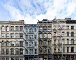 Exterior view of old apartment buildings in the SoHo neighborhood of Manhattan in New York City with empty blue sky background overhead Exterior view of old apartment buildings in the SoHo neighborhood of Manhattan in New York City with empty blue sky background overhead