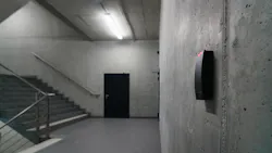 Concrete building stairwell with wall-mounted sensor in foreground and door in background. Concrete building stairwell with wall-mounted sensor in foreground and door in background.