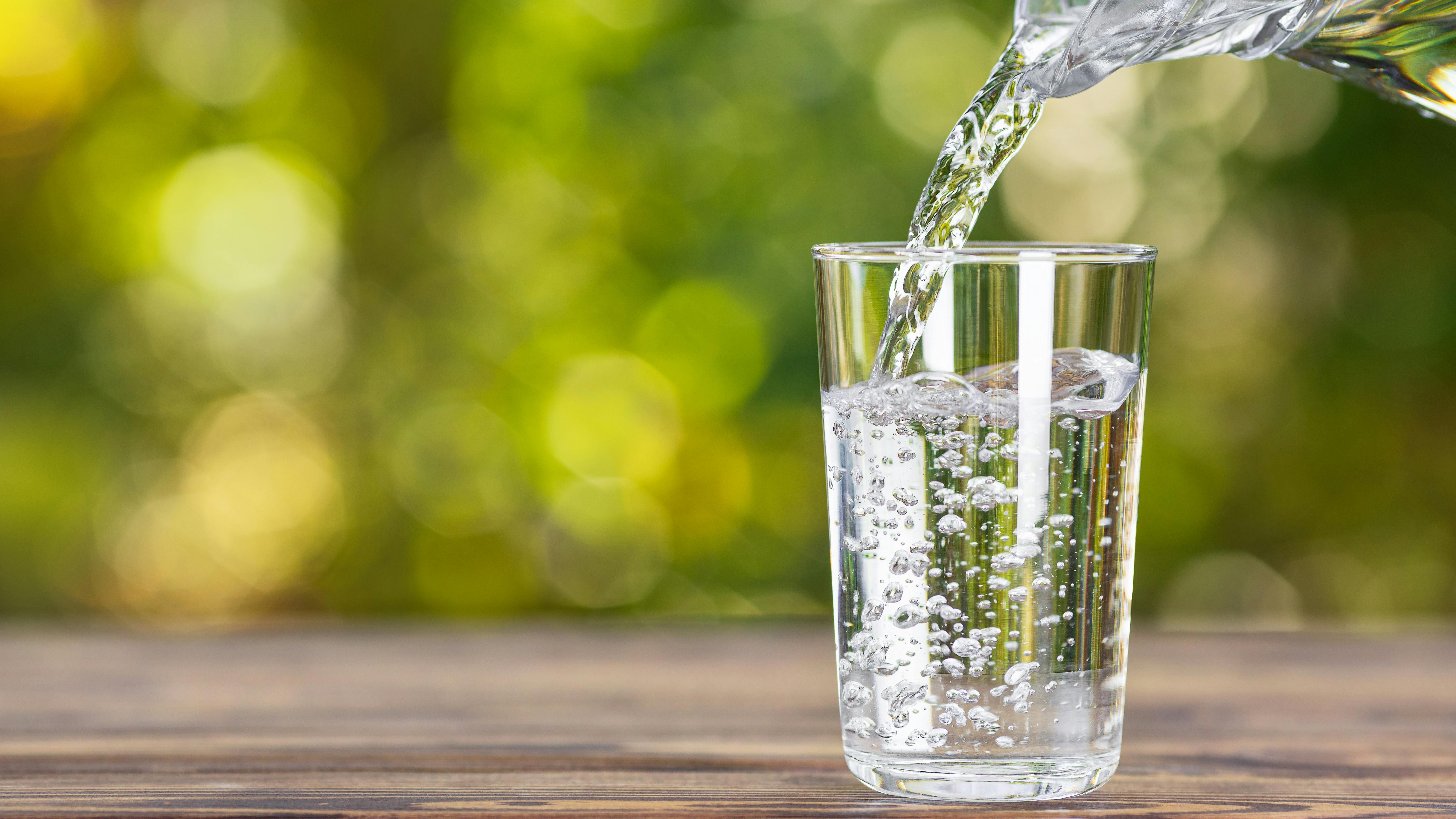 water from jug pouring into glass on wooden table outdoors