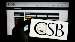 Person holding mobile phone with logo of federal agency U.S. CSB on screen in front of web page. F Person holding mobile phone with logo of federal agency U.S. CSB on screen in front of web page. F