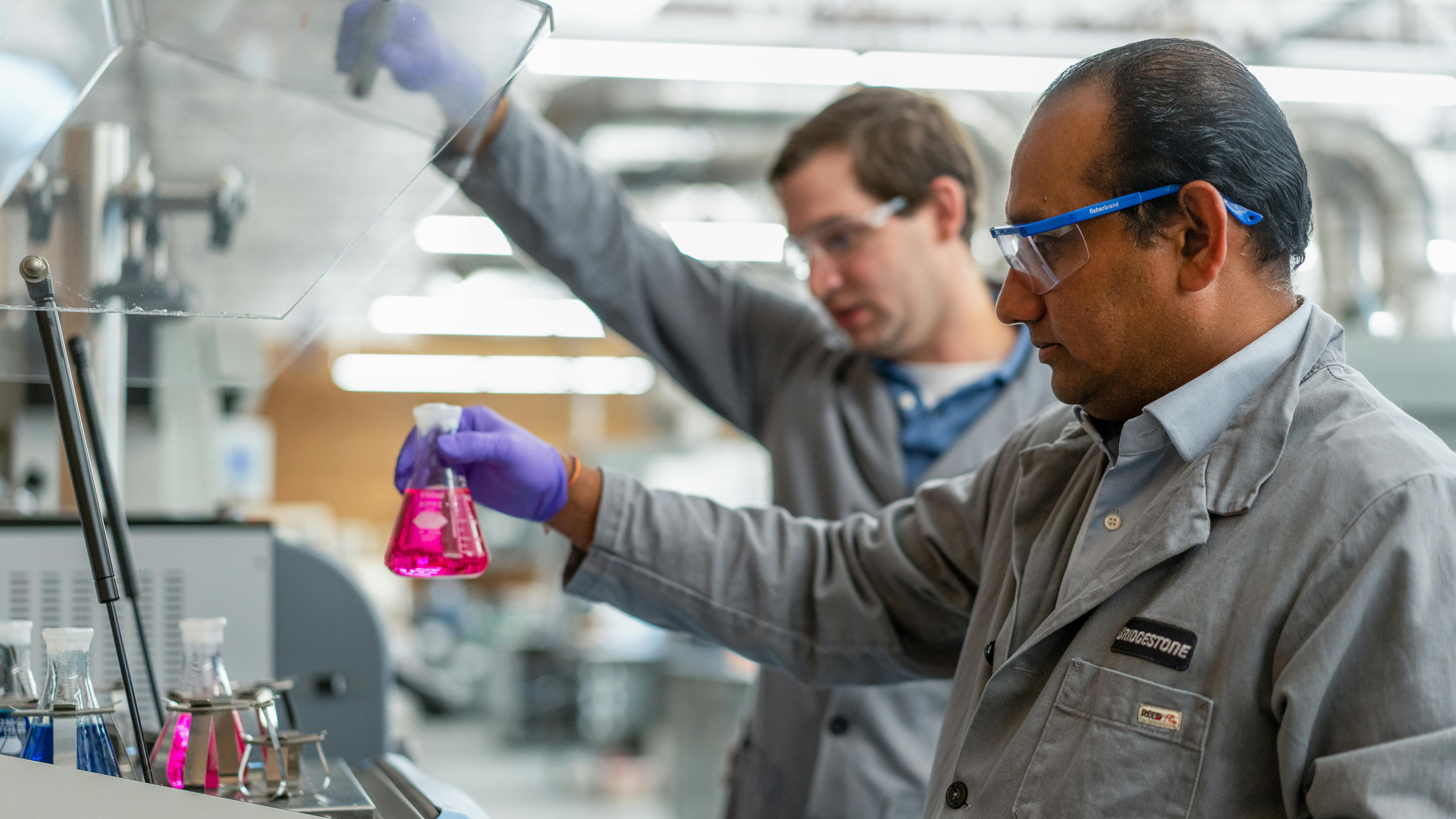 researchers handle Erlenmeyer flask with bring pink fluid