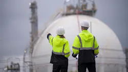 Engineers wearing safety gear, including hard hats with chemical plant in background Engineers wearing safety gear, including hard hats with chemical plant in background