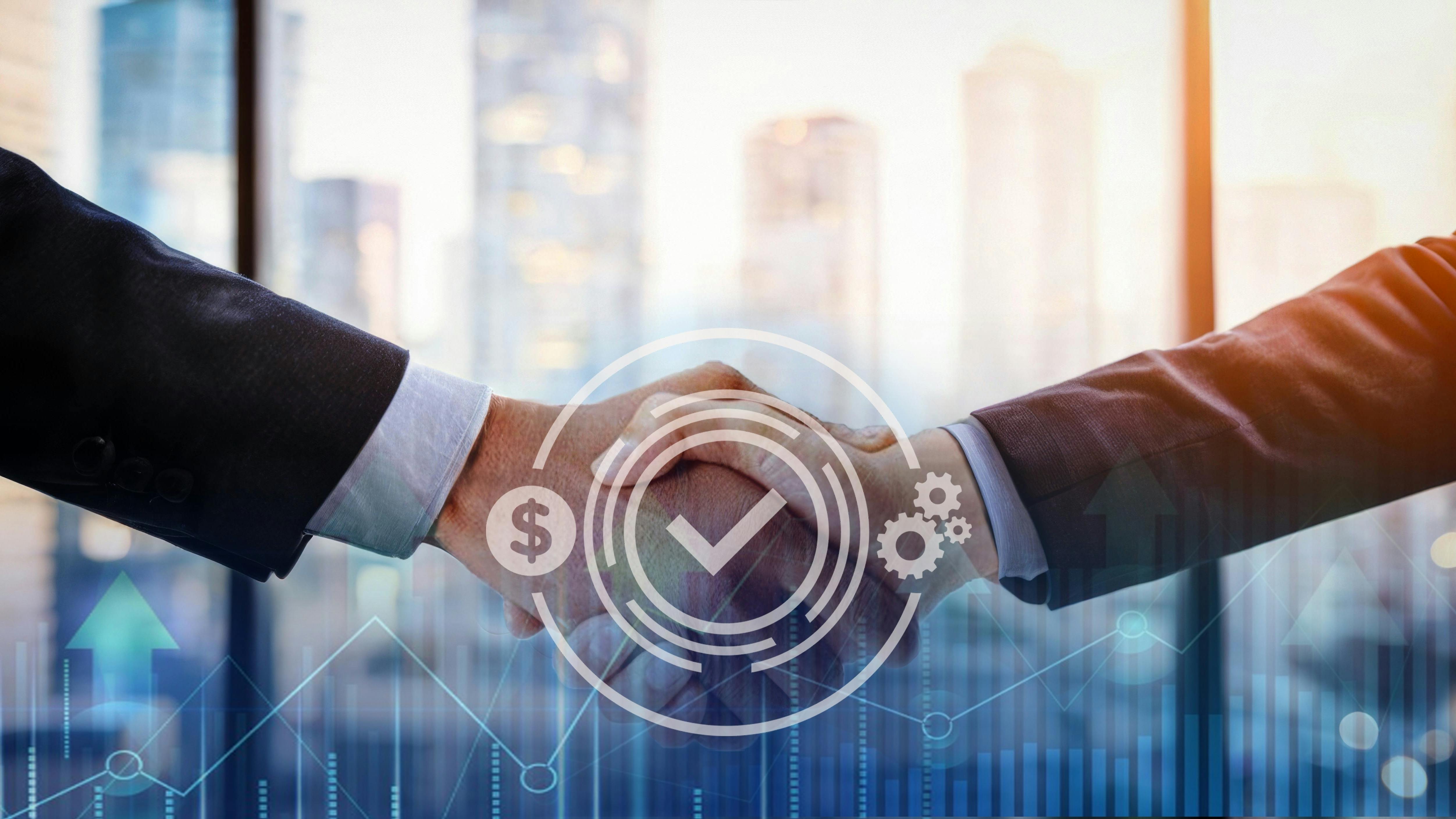 Two business professionals in formal attire shaking hands across a table, symbolizing partnership or successful agreement in a modern office setting.