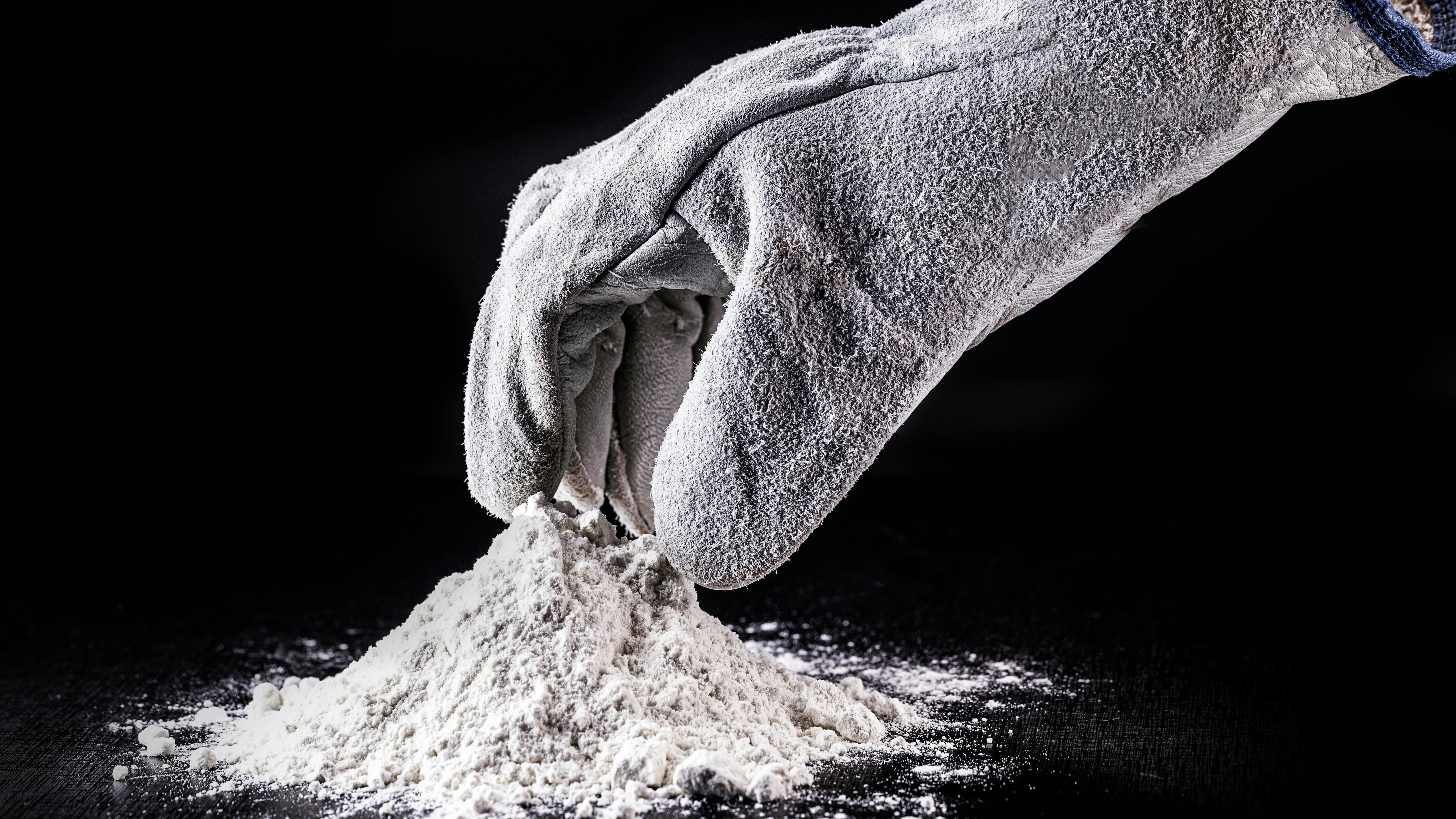 gloved hand reaches into small pile of powder surrounded by black background