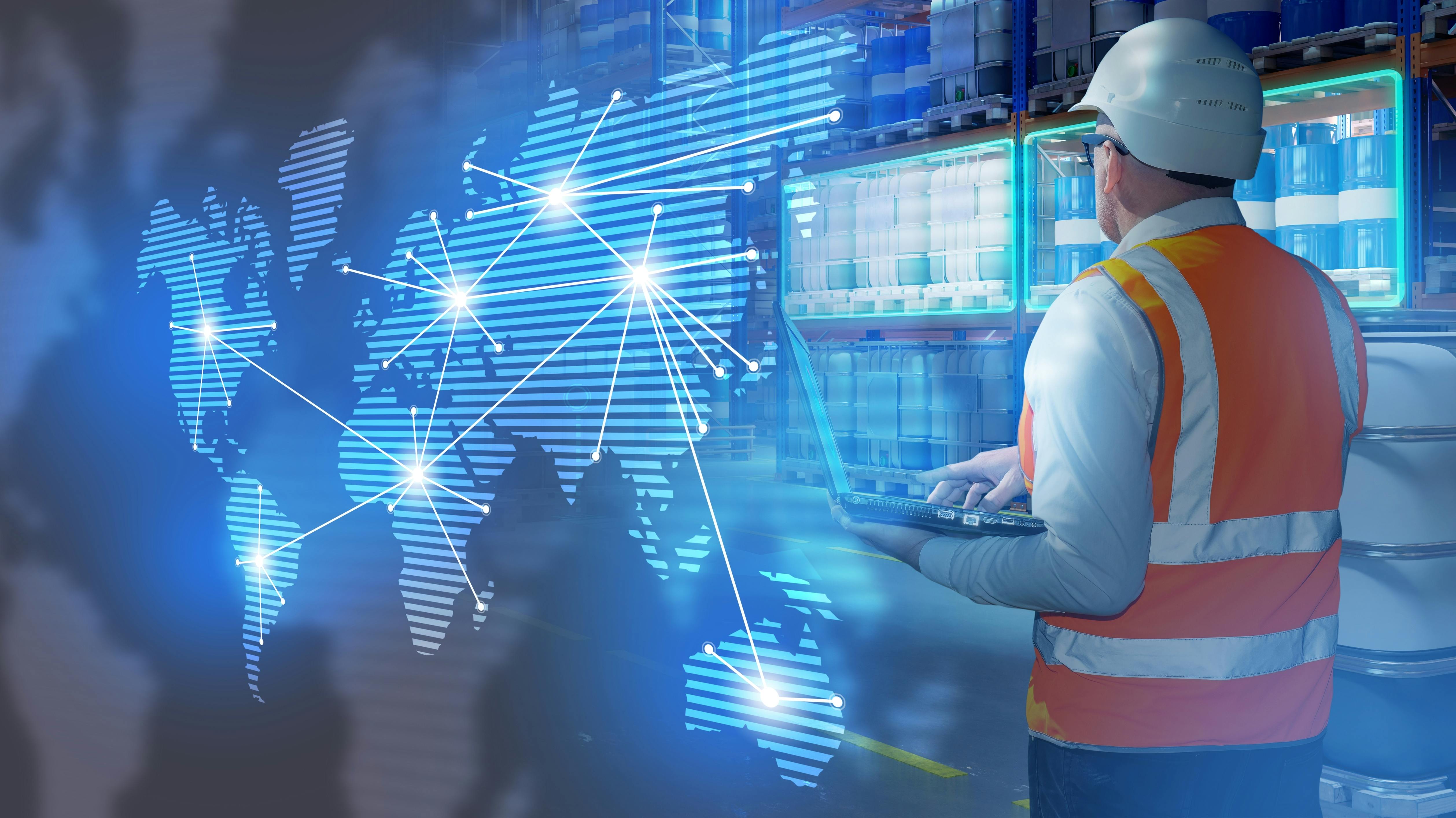 Warehouseman stands in warehouse with barrels. International logistics supply chains. Man logistician holding laptop with his back to camera.