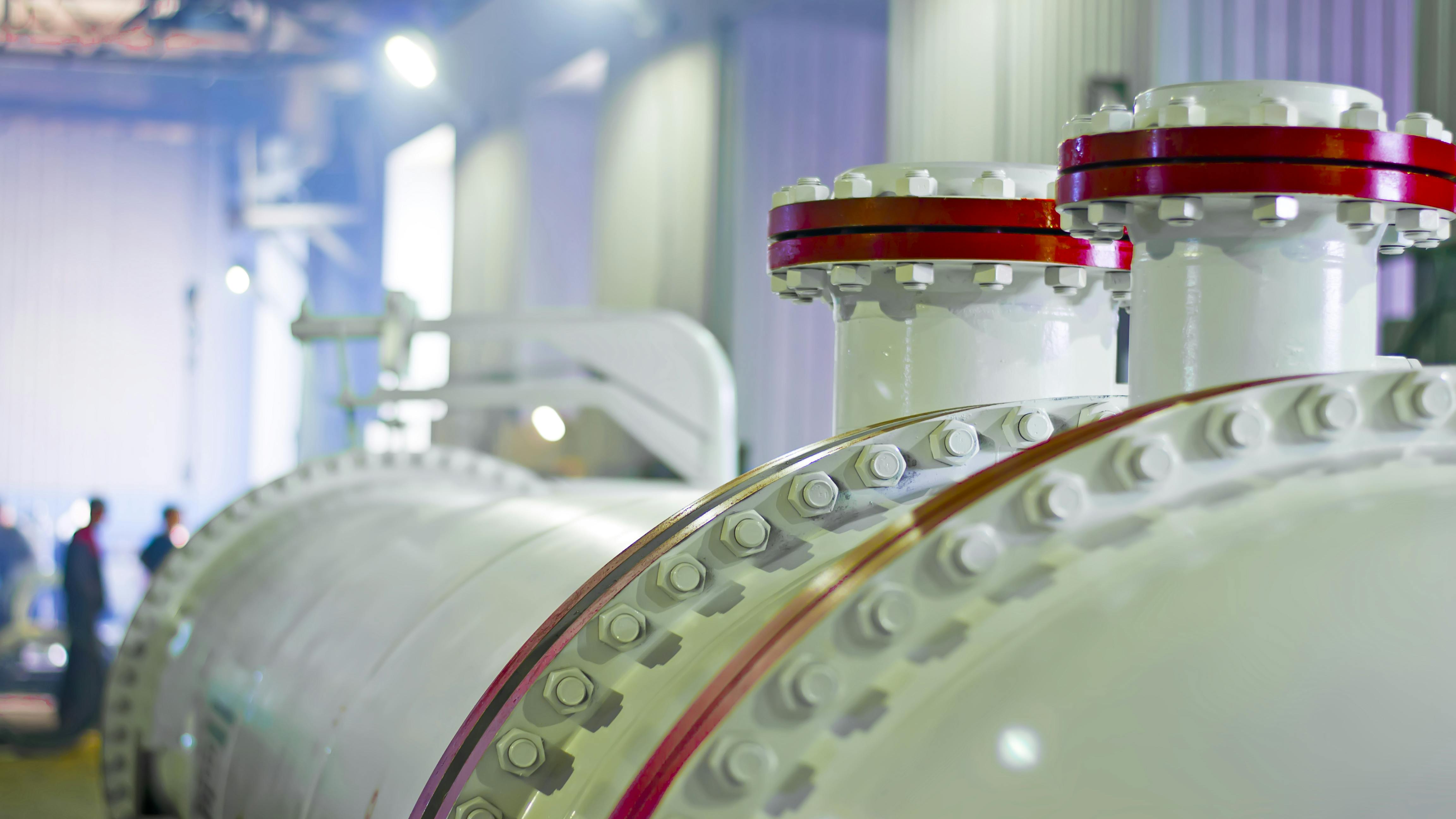 closeup shot of heat exchanger inside plant with people walking in background