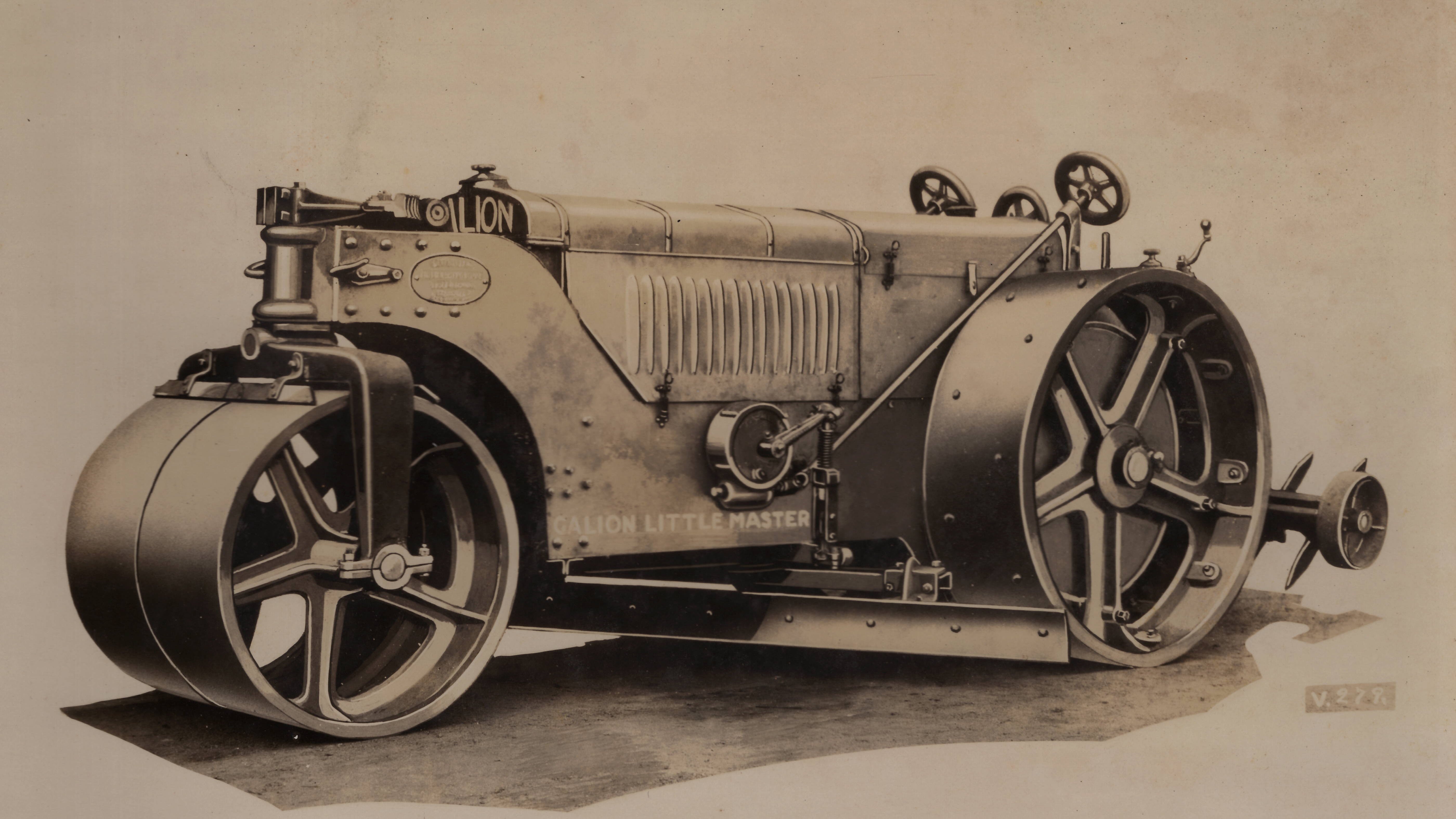 The introduction of internal combustion to rollers made it possible to equip them with attachments for road maintenance. This Galion Little Master three-wheel roller is outfitted with a rear scarifier to break up packed surfaces, and an adjustable underframe moldboard to strike the surface off as it compacted. The projections on the large drive drums provide additional traction; these are rather subtle, as various spikes and cleats were also available, all mounting through holes in the drums. Equipped with stout enough traction enhancements, a suitably powerful three-wheel roller could also draw some sizes of pull graders in lieu of, or even in addition to, the underframe blade.