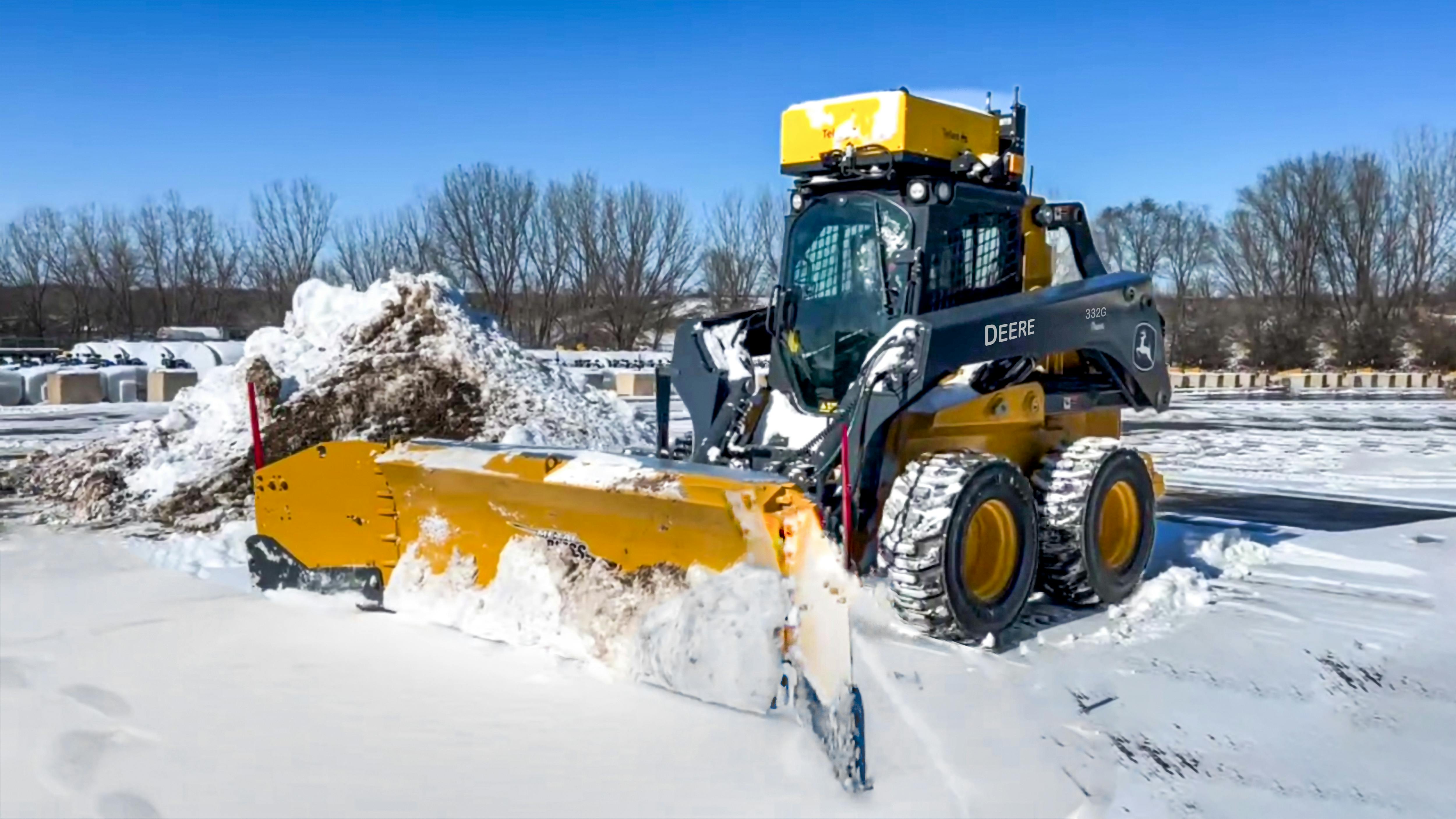 A Deere 332G skid steer with a snow plow for remote operation.