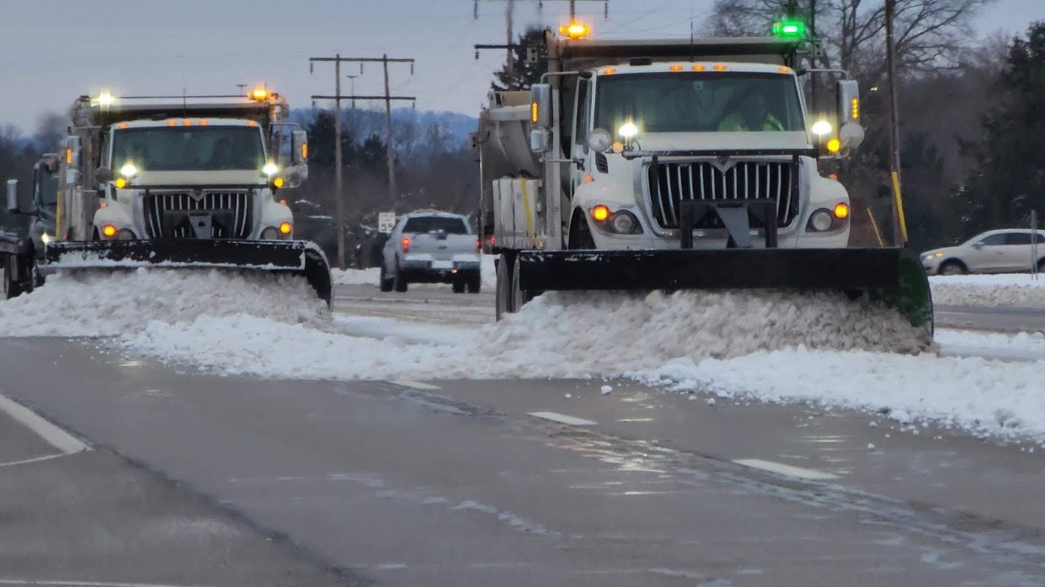 A trio of single-rear-axle plow trucks sporting green and amber strobes cleans a stretch of Ohio highway after a storm has passed. Green lights are used only on snowplows, differentiating them from other road-maintenance equipment with amber-only lights.