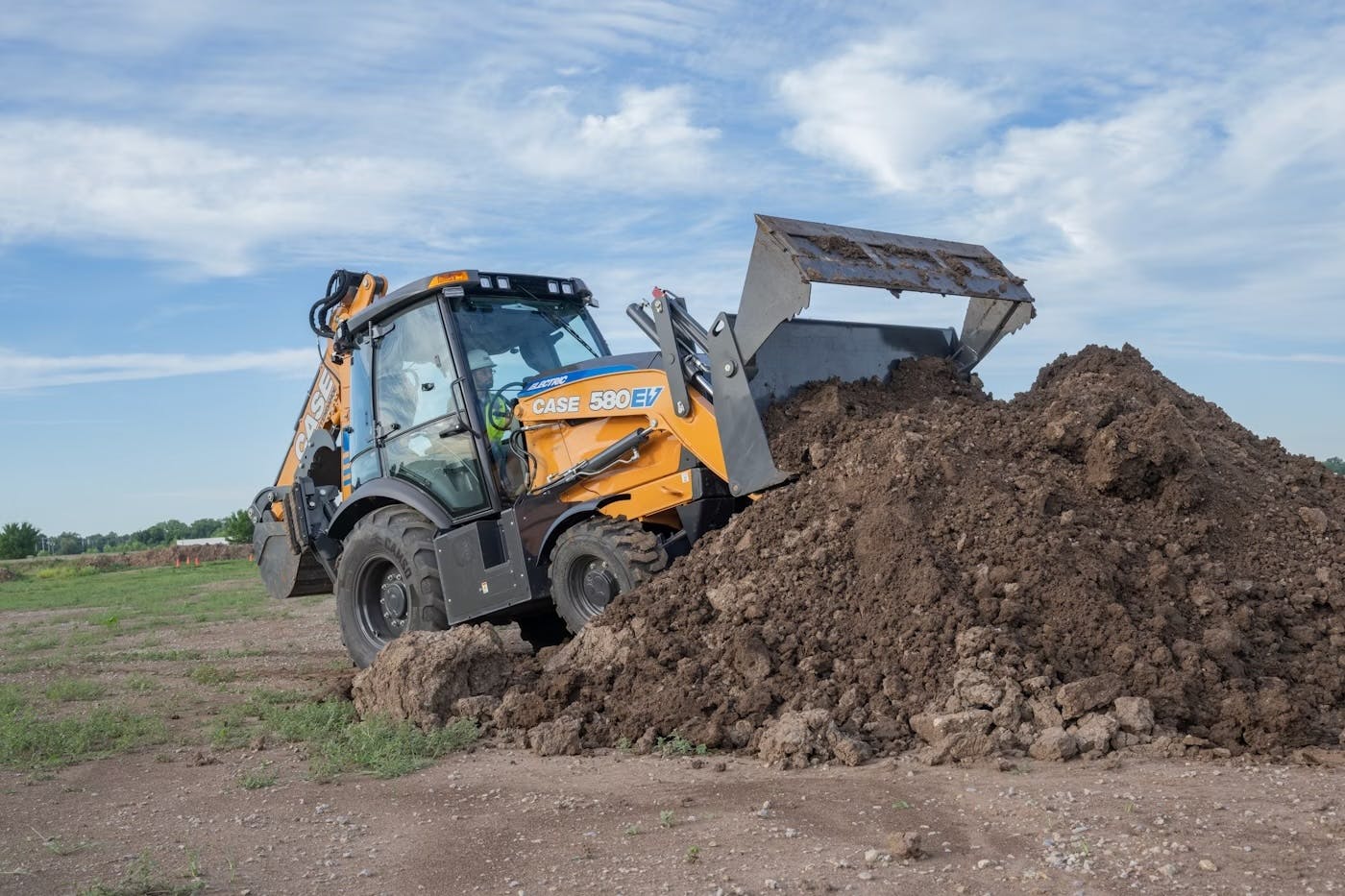 Case Construction Equipment's 580 EV Electric Backhoe dumping dirt in a pile.