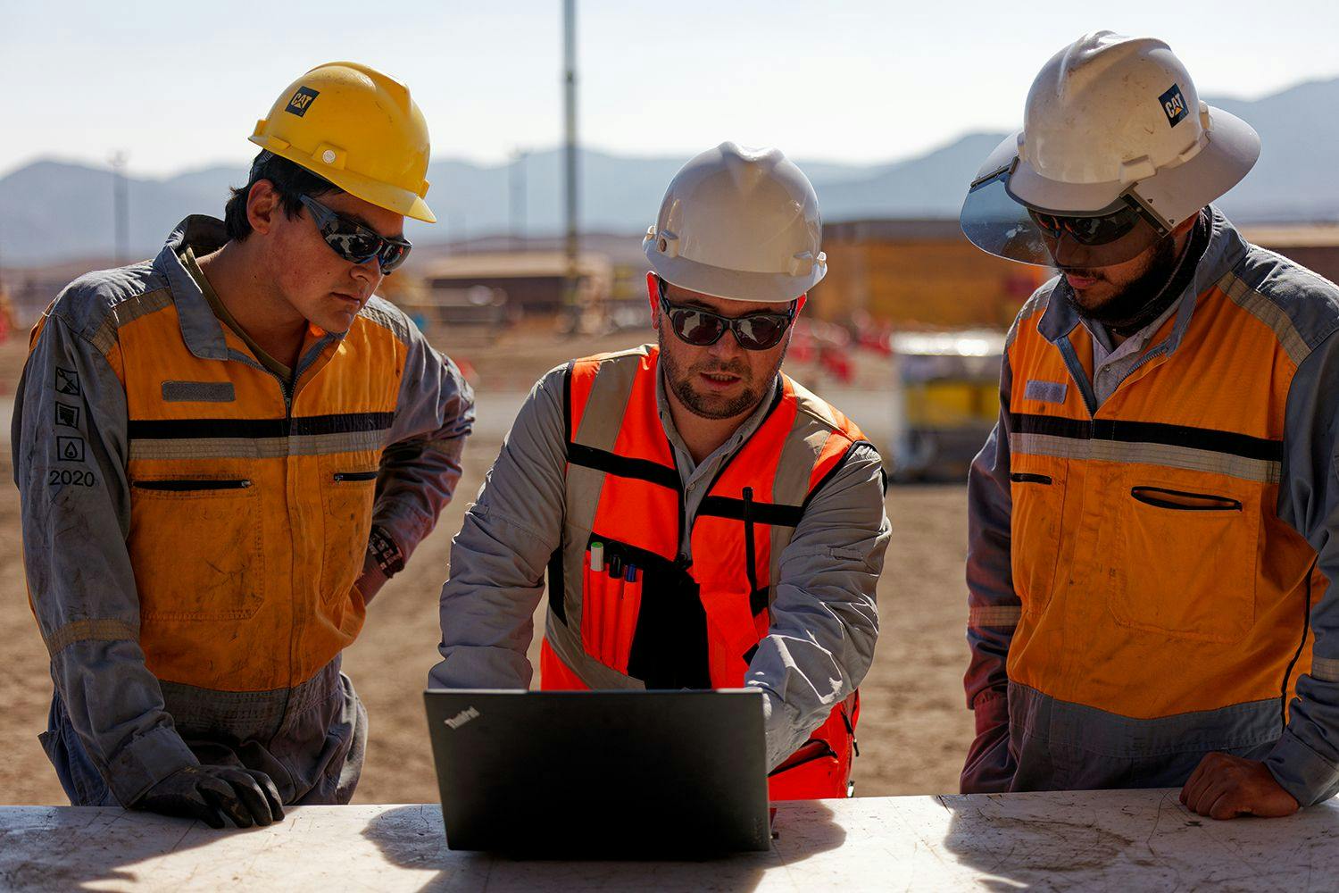 Contractors with Cat helmets look at a laptop.