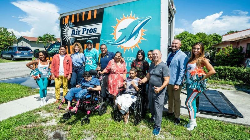 Families that have received home AC systems, Air Pro employees and Miami Dolphins cheerleaders pose for photo.