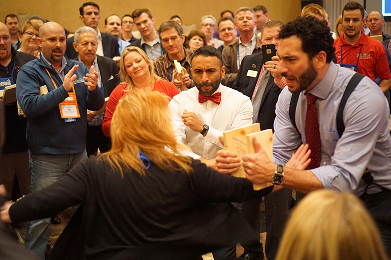 Nexstar member Tammy Ferris breaking through a board held by Keith Mercurio while Nexstar Training Manager Julian Scadden and the crowd cheer her on