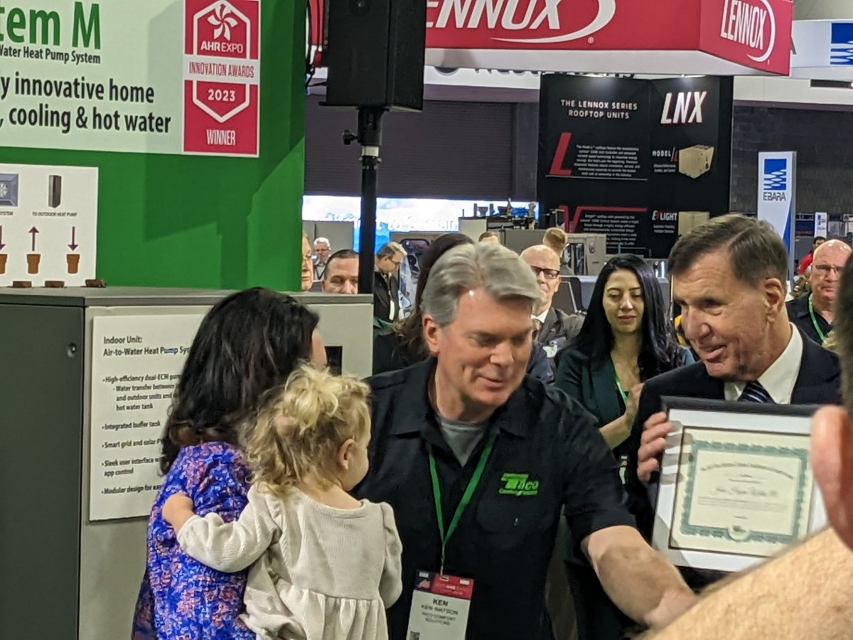 Dan Holohan (at right) presents the award to Hazen III's wife, Katelyn, and their daughter, Madison Marie at the 2023 AHR Expo.
