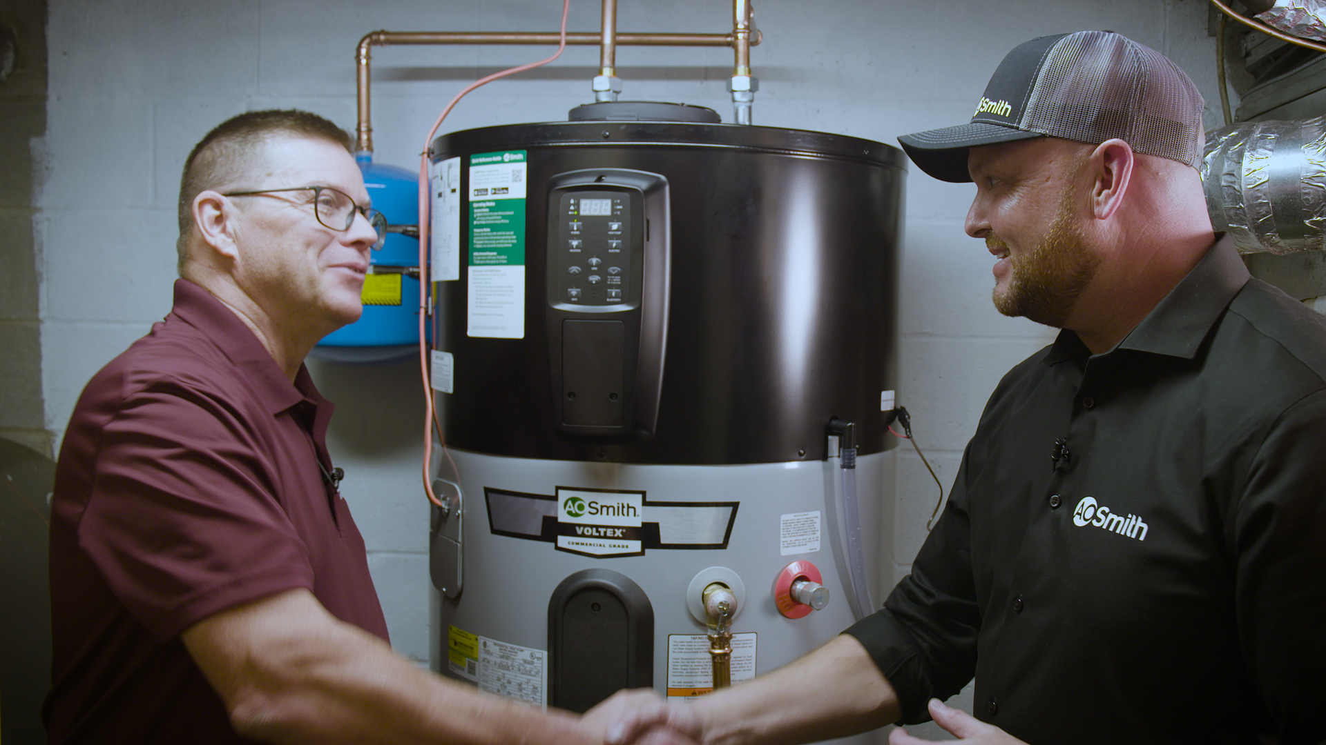 Gerry Winset of A.O. Smith (right) shakes hands with Carl (left), a tech working with W. L. Staton Plumbing, Cooling & Heating, in front of a Voltex hybrid electric heat pump water heater.