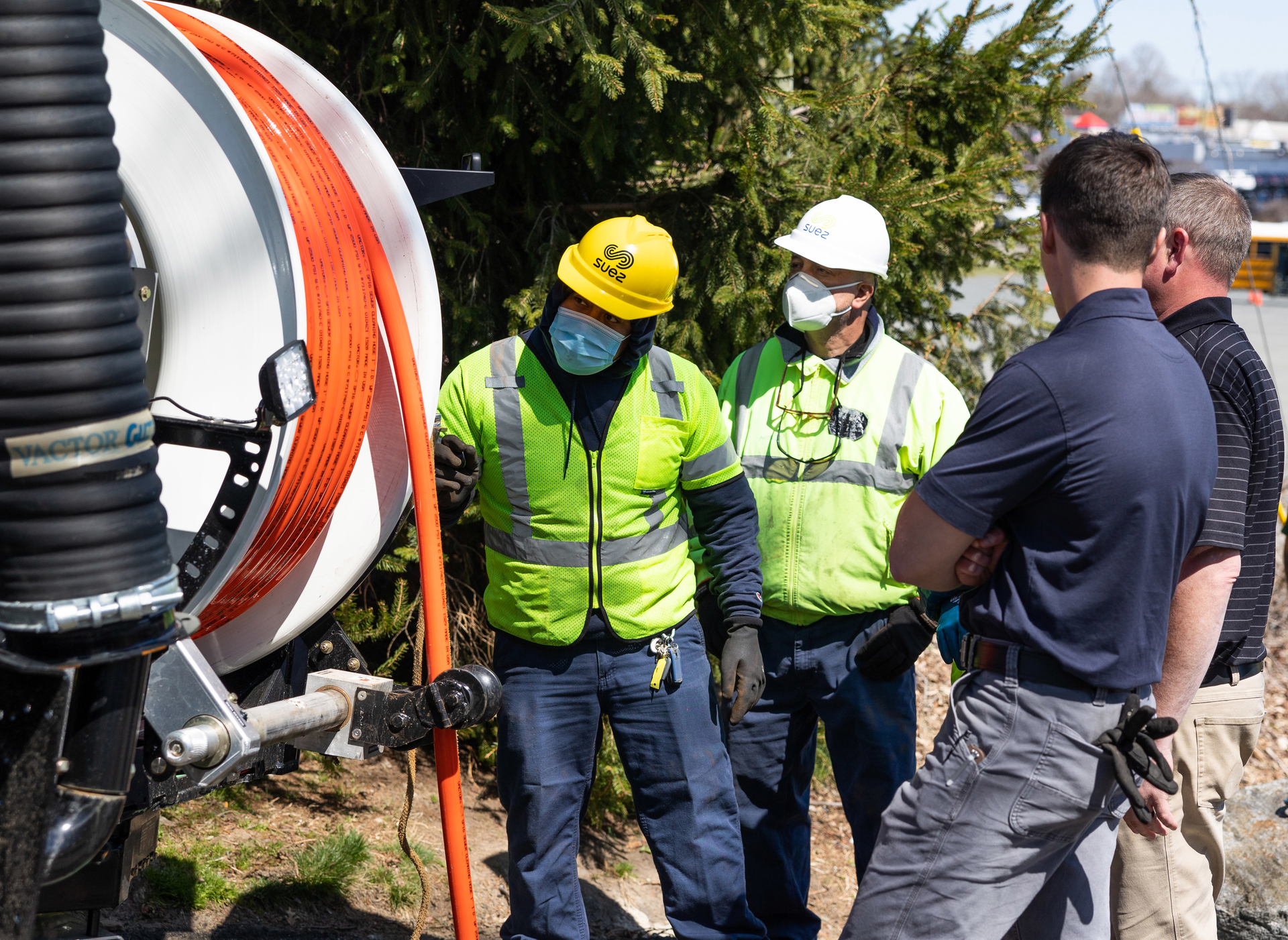 Workers wearing their PPE at the vacuum truck. To prevent free spooling the nozzle up the line and losing control, use a nozzle skid and hold the nozzle back.