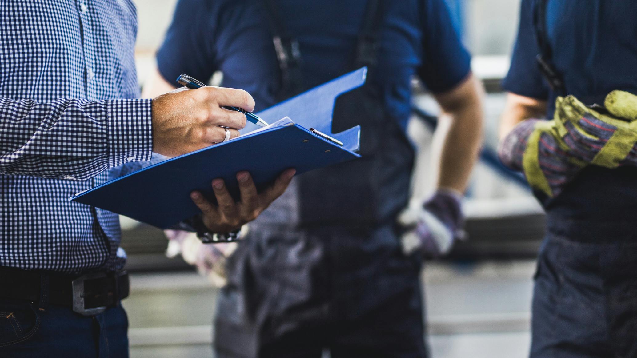 Unrecognizable owner going through reports with two workers in a warehouse.