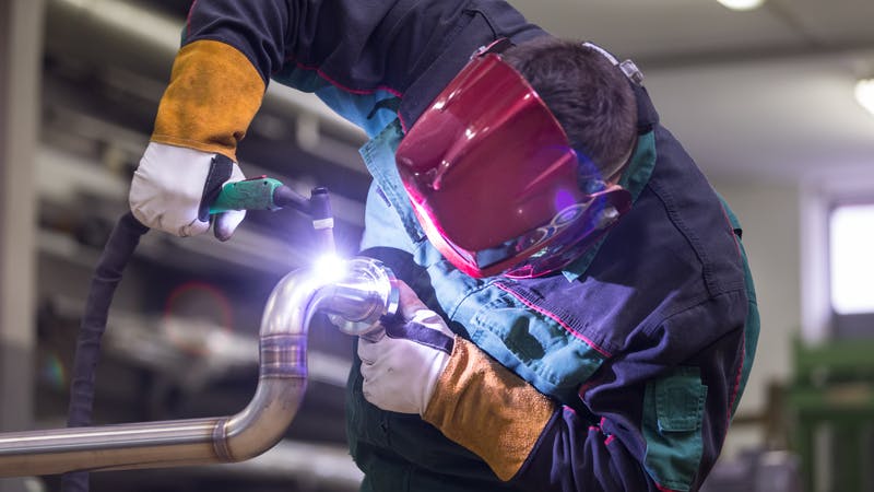 Industrial worker welding in metal factory.