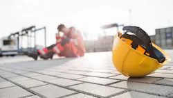 Yellow hardhat at shipyard with depressed male worker in background Yellow hardhat at shipyard with depressed male worker in background