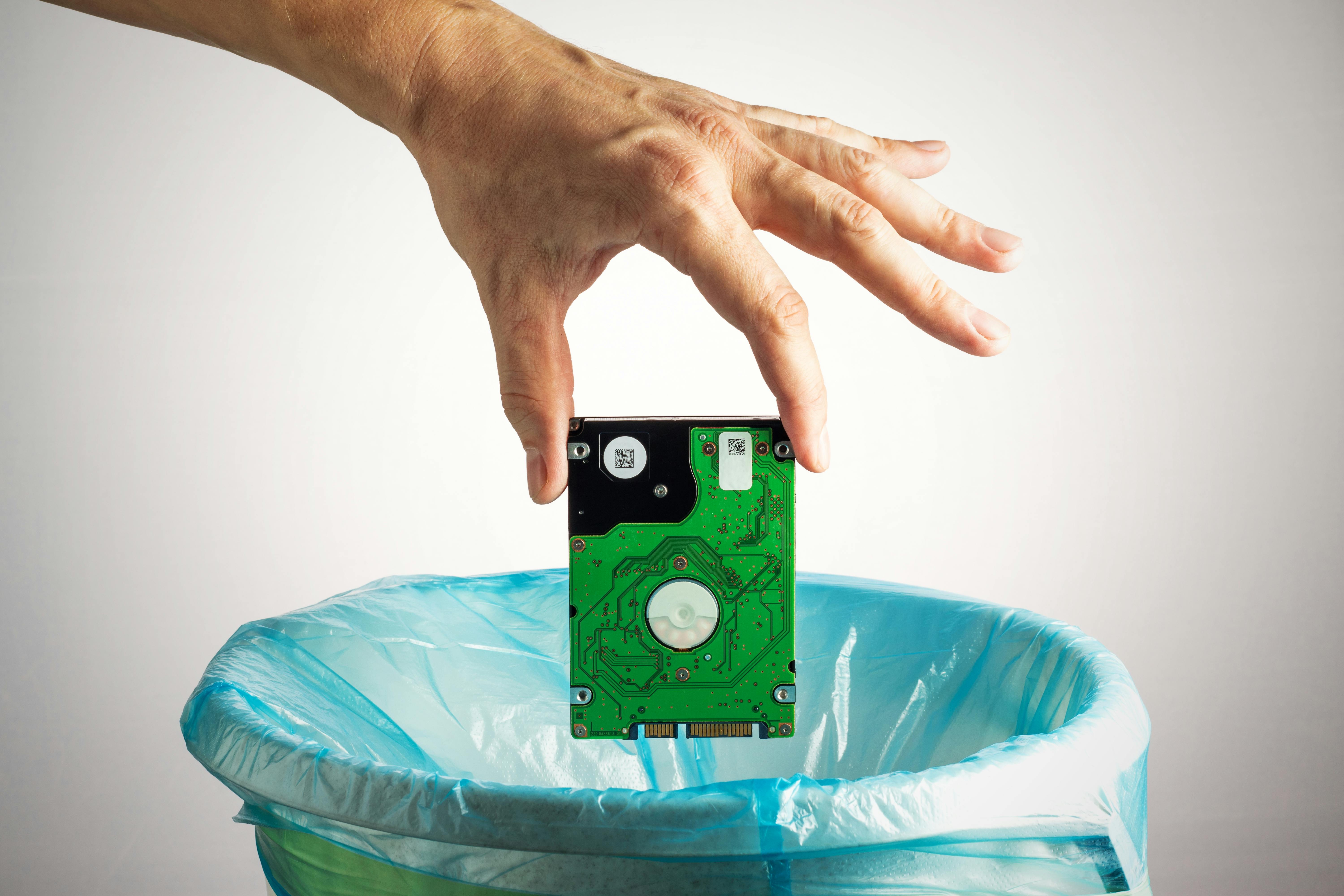 Person's hand throws a computer hard disk into the trash bin