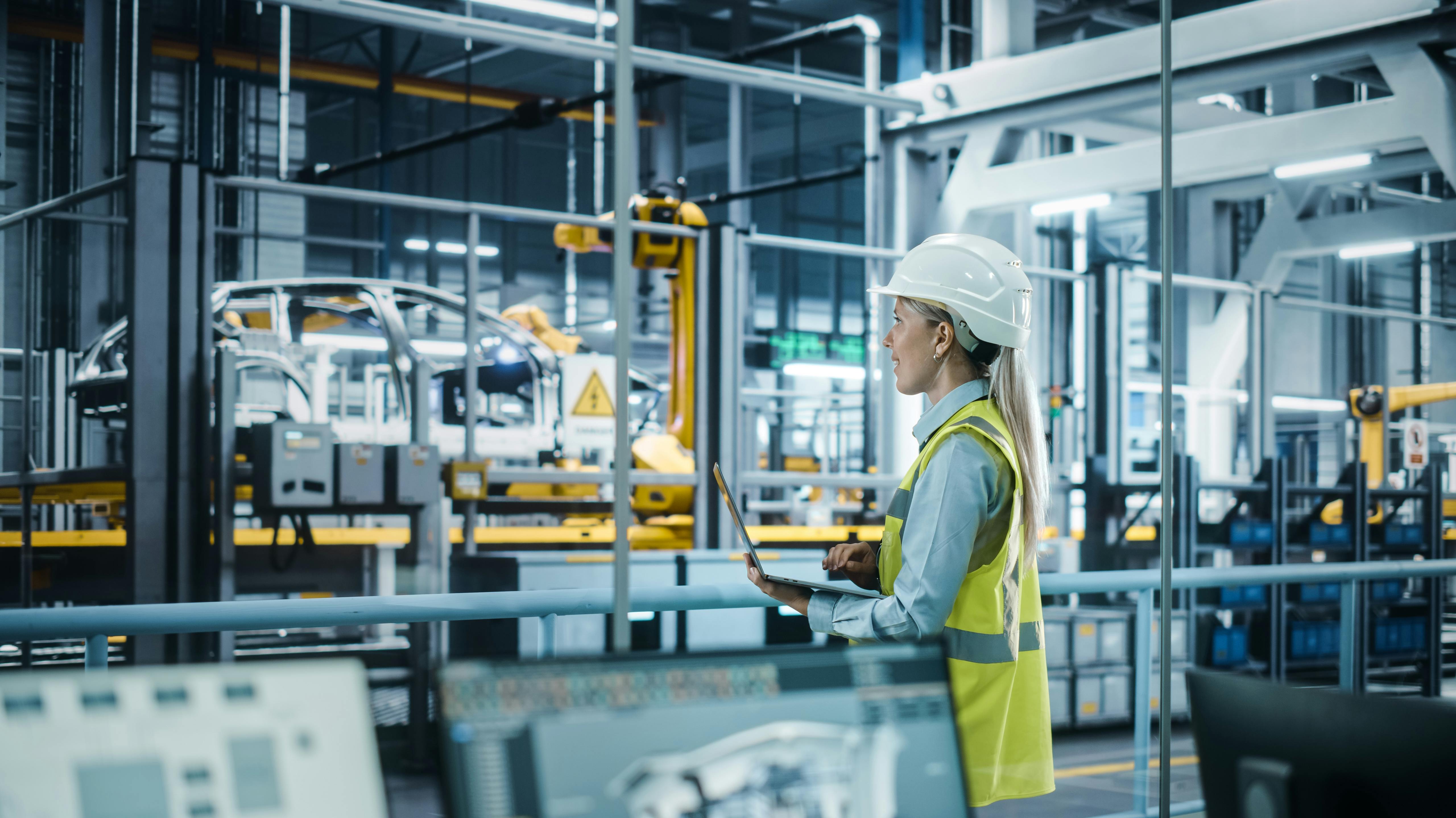 Car Factory: Female Automotive Engineer Wearing Hard Hat, Standing, Using Laptop