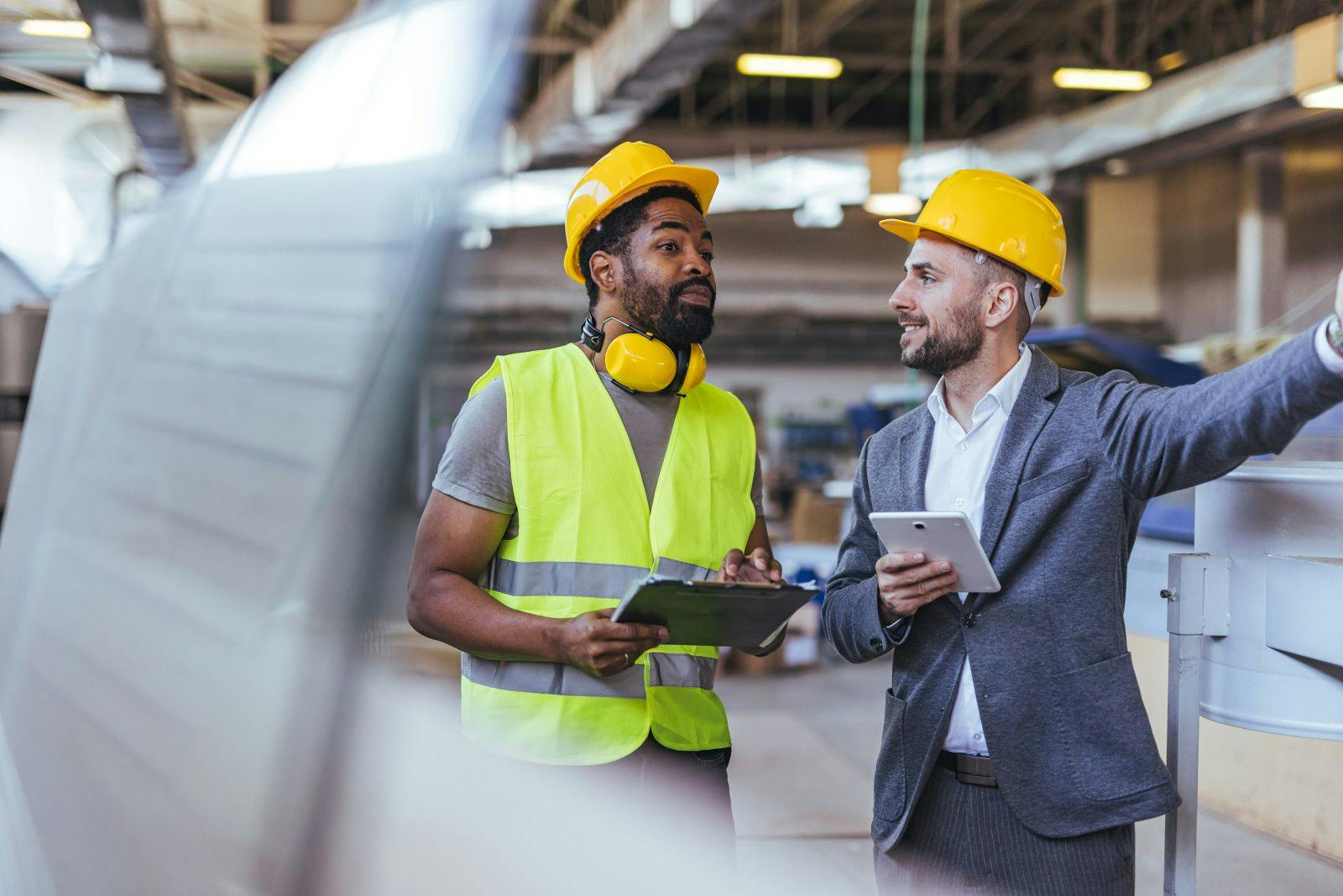 A skilled laborer and a supervisor engage in a discussion to coordinate production plans within a factory setting, emphasizing teamwork, communication, and a professional atmosphere.
