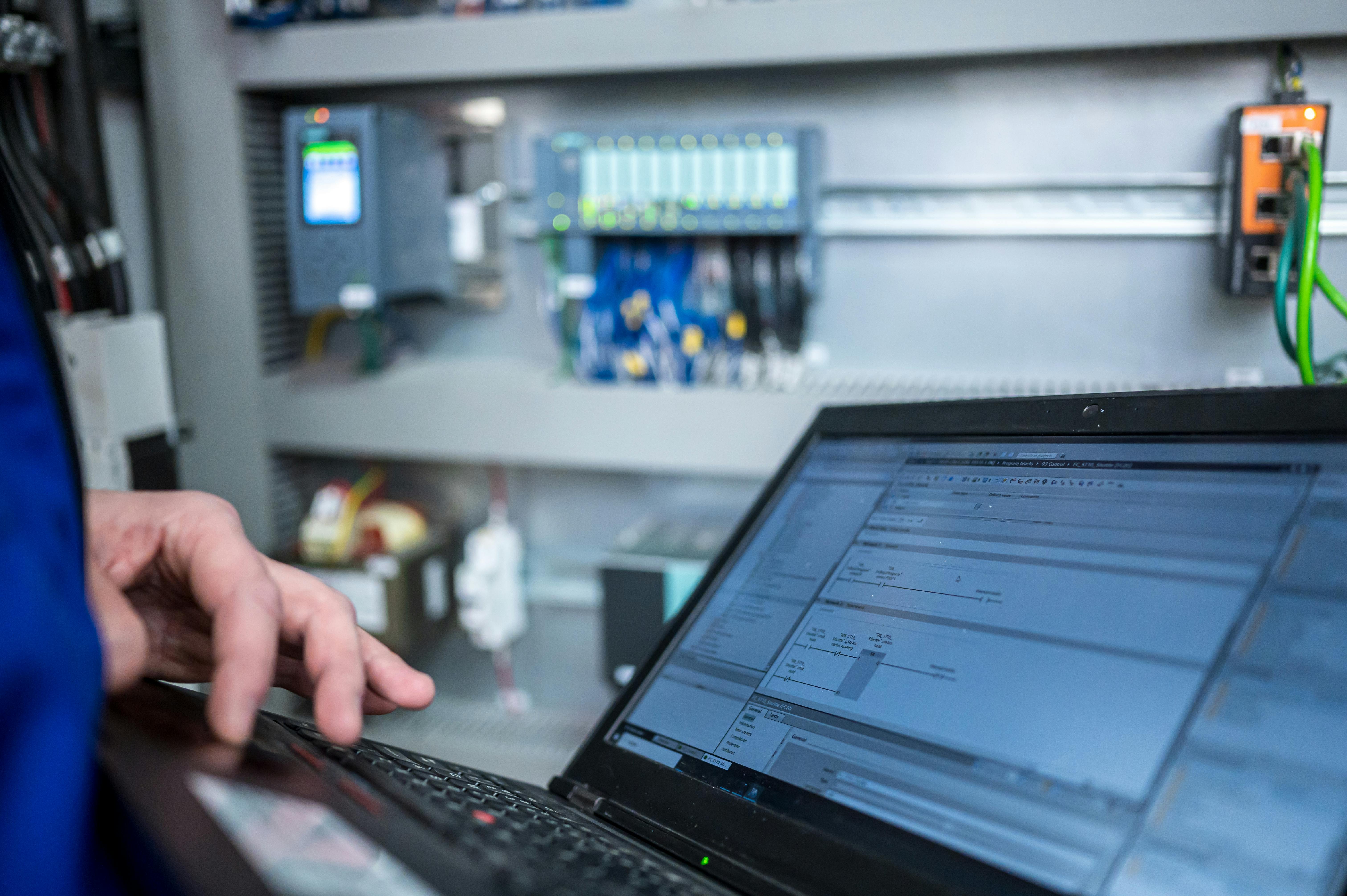 Programmer of PLC checks correct function of program in PLC with electrical cabinet in background