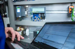 Programmer of PLC checks correct function of program in PLC with electrical cabinet in background Programmer of PLC checks correct function of program in PLC with electrical cabinet in background