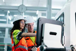 Two workers in orange vests are working on a machine. One of them is pointing at a screen Two workers in orange vests are working on a machine. One of them is pointing at a screen