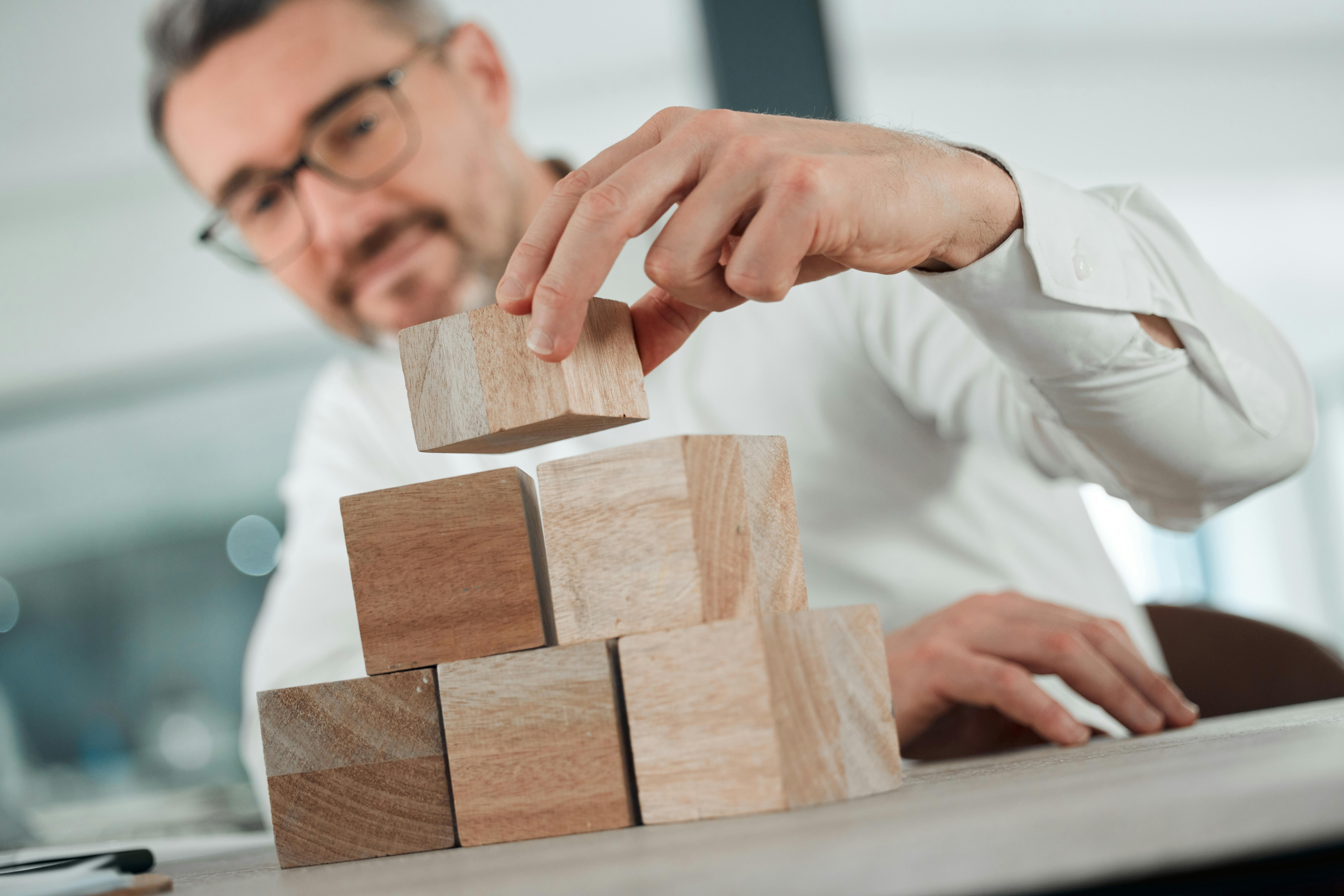 Start building your future from now. Shot of an unrecognisable businessman sitting alone in his office and using building blocks to plan.