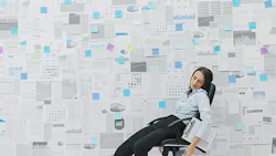 woman asleep on a chair in front of wall of business papers woman asleep on a chair in front of wall of business papers