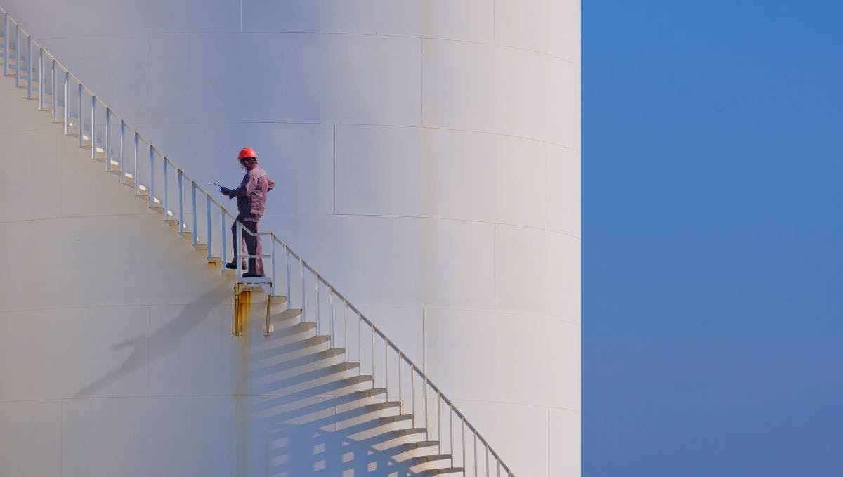 Engineer is walking up spiral staircase to working on top of fuel tank