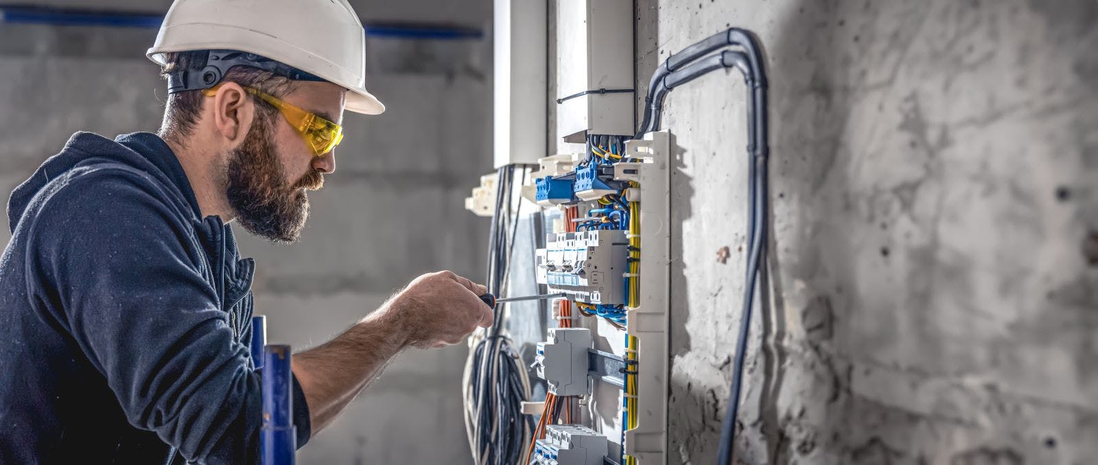 A male electrician works in a switchboard with an electrical connecting cable.
