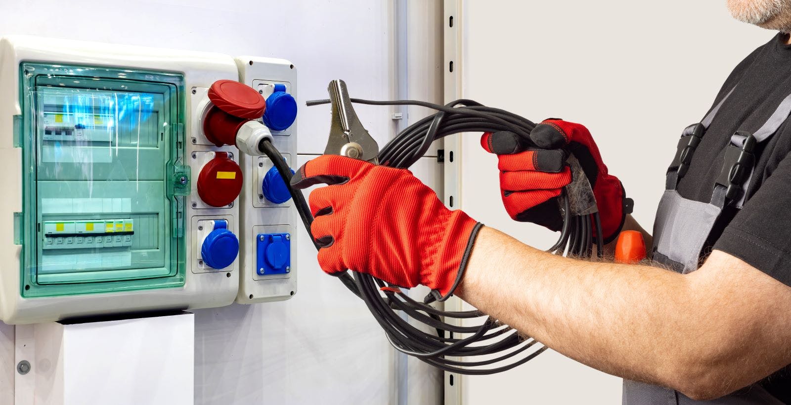 Electrician connects a high-power cable to an industrial socket panel, performing setup tasks related to electrical installation and temporary power distribution systems.