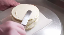 Female professional hands levels cream on baked sponge cake using metallic pastry scraper Female professional hands levels cream on baked sponge cake using metallic pastry scraper