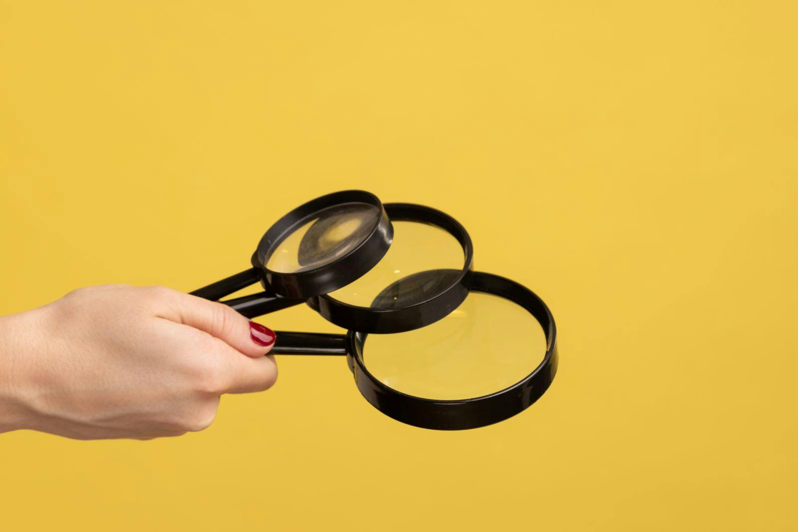 Profile side view closeup of woman hand holding several magnify glasses, loupe. Indoor studio shot isolated on yellow background.